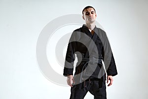 Cool guy in black kimono fighter posing in karate stance on white studio background with copy space
