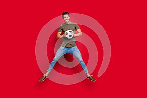 Cool guy jumping high holding ball celebrating first place competitions wear casual outfit isolated on red background