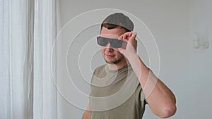 Cool guy with stylish sunglasses poses for camera by wall