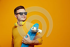 Cool guy wearing yellow jumper and sunglasses holding longboard and looking at free empty space