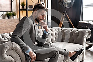 Cool and handsome. Good looking young man in full suit sitting on the sofa while spending time indoors.