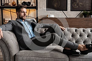 Cool and handsome. Good looking young man in full suit sitting on the sofa while spending time indoors.