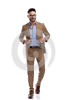 Cool handsome guy with eyeglasses buttoning suit and walking