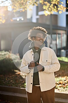 Cool happy young African American guy standing at big city sunny street.