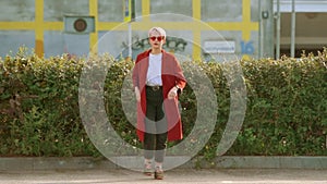 Cool hipster Ñaucasian student girl wearing red coat and red round glasses dancing in the street