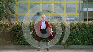 Cool hipster Ñaucasian student girl wearing red coat and red round glasses dancing in the street