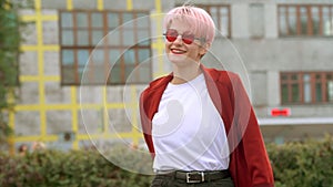 Cool hipster Ñaucasian student girl wearing red coat and red round glasses dancing in the street