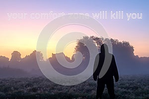 A cool hipster motivation phrase to inspire. A hooded figure outdoors looking at a sunrise with the phrase `Your comfort zone wil