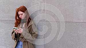 Cool hipster teen girl red hair standing on city urban street using cell phone.