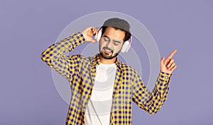 Cool Indian guy in headphones enjoying his favorite music on lilac background