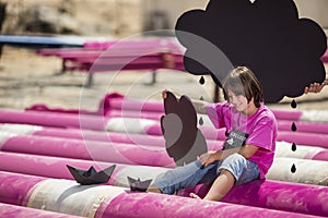 Cool kid plays on a pink pipes with black paper boats and clouds on construction site