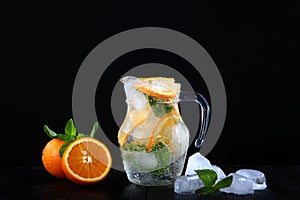 Cool lemonade made from oranges and mint in a glass jug. Ice cubes in the drink. Photo on a black background. Copy of the space