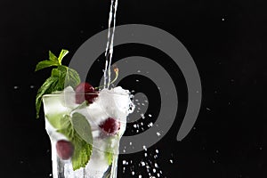 Cool lemonade is poured into a glass with cherries and ice. Mint leaves in a glass. Seasonal summer drink. Photo on a black