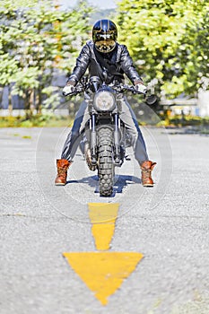 Cool looking motorcycle rider on custom made scrambler style cafe racer on the road with an arrow sign photo