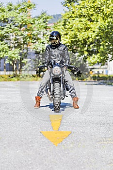 Cool looking motorcycle rider on custom made scrambler style cafe racer on the road with an arrow sign