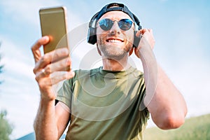 Cool man in baseball cap, wireless headphones and blue sunglasses browsing in his mp3 player playlists smartphone device and