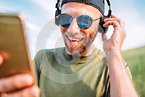 Cool man in baseball cap, wireless headphones and blue sunglasses browsing in his mp3 player playlists smartphone device and