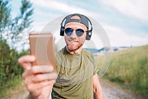 Cool man in a baseball cap, wireless headphones and blue sunglasses browsing in his mp3 player playlists smartphone device,