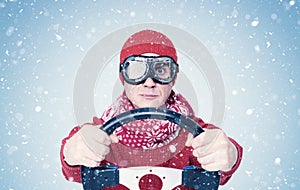 Cool man in red sweater scarf and hat with stylish goggles, drives a car in snow with his hands on the steering wheel. Front view