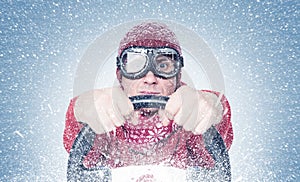 Cool man in red sweater scarf and hat with stylish goggles, drives a car in snowstorm with his hands on the steering wheel. Front