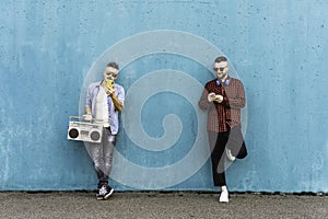 Cool men looking at mobile phone lean against blue wall - Couple of influencer guys listening music with vintage boombox stereo