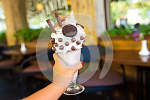 Cool milkshake with cookies and chocolate balls. Milkshake in a glass beaker on a table on a street platform in a cafe. Refreshing