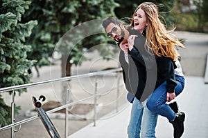 Cool multiracial couple posing with longboard. European girl jumped over shoulder arabian man