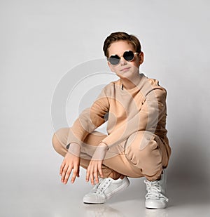 Cool preteen boy child feeling happy squatting over studio wall