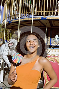 Cool real teenage girl with candy near carousels at amusement park walking, having fun