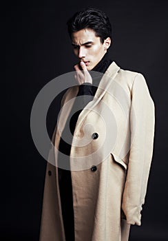 Cool real young handsome man in coat on black background posing, fashion people concept