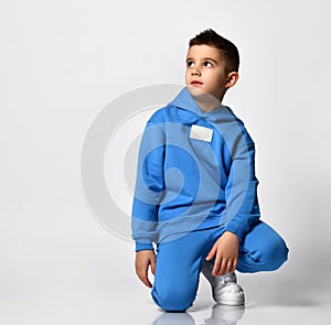 Cool schoolboy in trendy bright blue sportswear sitting on a white background.