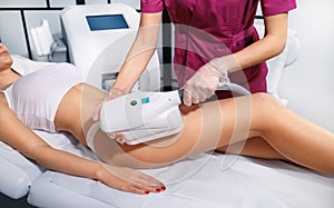 Young woman getting cryolipolyse treatment in cosmetic cabinet. Fat freezing technology on legs. Cool sculpting procedure photo