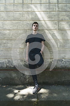 Cool, standing young man who is leaning against a wall