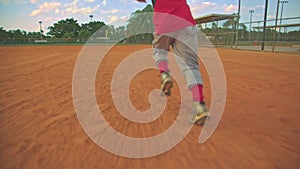 Cool steadicam shot of kid running to first base on baseball field. Shot from behind him