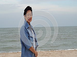Cool stylish Asian senior woman smiling happy at beach jean jacket fashion cloth