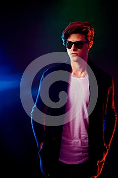 Cool stylish man in black jacket and sunglasses. High Fashion male model in colorful bright neon lights posing on black
