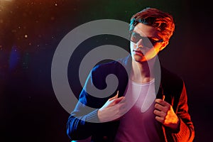 Cool stylish man in black jacket and sunglasses. High Fashion male model in colorful bright neon lights posing on black