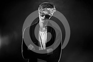 Cool stylish man in black jacket and sunglasses. High Fashion male model posing on black background.