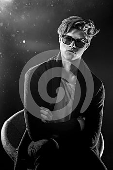 Cool stylish man in black jacket and sunglasses. High Fashion male model posing on black background.