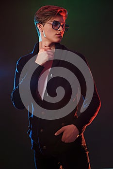 Cool stylish man in black jacket and sunglasses. High Fashion male model posing on black background.