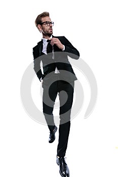 Cool stylish man in black suit looking to side and fixing tie