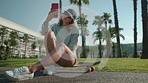 cool teen girl is taking selfie with longboard by smartphone in summer day on city street
