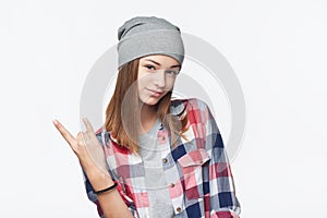 Cool teen girl wearing checkered shirt and beanie hat gesturing rock sign