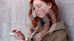 Cool teen redhead girl standing on city urban street using cell phone.