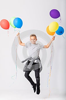 Cool teenage boy holding a bunch of balloons jumps in an empty room