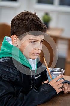Cool teenage boy sits in coffee and drinks fruit juice