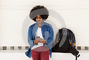 Cool travel guy sitting with mobile phone and bag