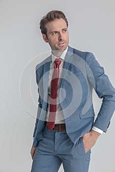 Cool unshaved man in blue suit holding hand in pocket and looking to side