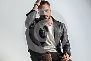 Cool unshaved man with wet hair holding elbow on knee and posing