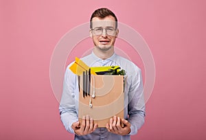 Cool upset hipster in a sky blue shirt and computer glasses stands with a cardboard box with different things